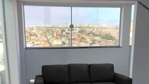 A modern living room with a large window offering a city view. - Best Location in Rio Vermelho, walking distance to the beach and fun (Salvador)