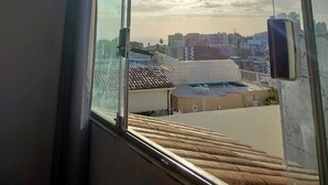 A view from a window with a metal railing, overlooking a cityscape with buildings and a clear sky. - Best Location in Rio Vermelho, walking distance to the beach and fun (Salvador)