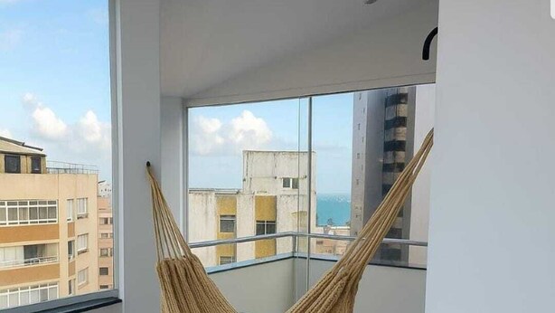 A balcony with a hammock, large windows, and a view of buildings and the sea. - Best Location in Rio Vermelho, walking distance to the beach and fun (Salvador)