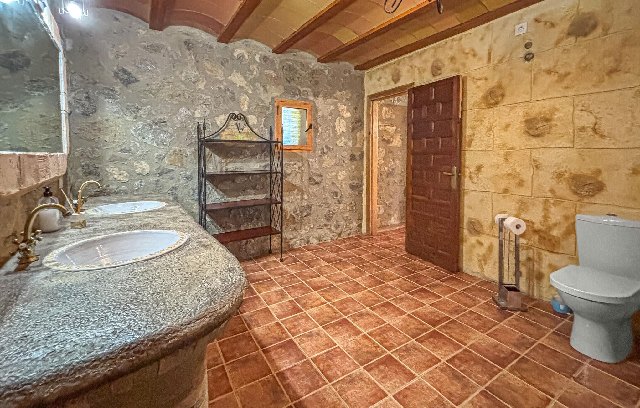 Un baño con paredes de piedra, dos lavamanos, una puerta de madera y un inodoro.