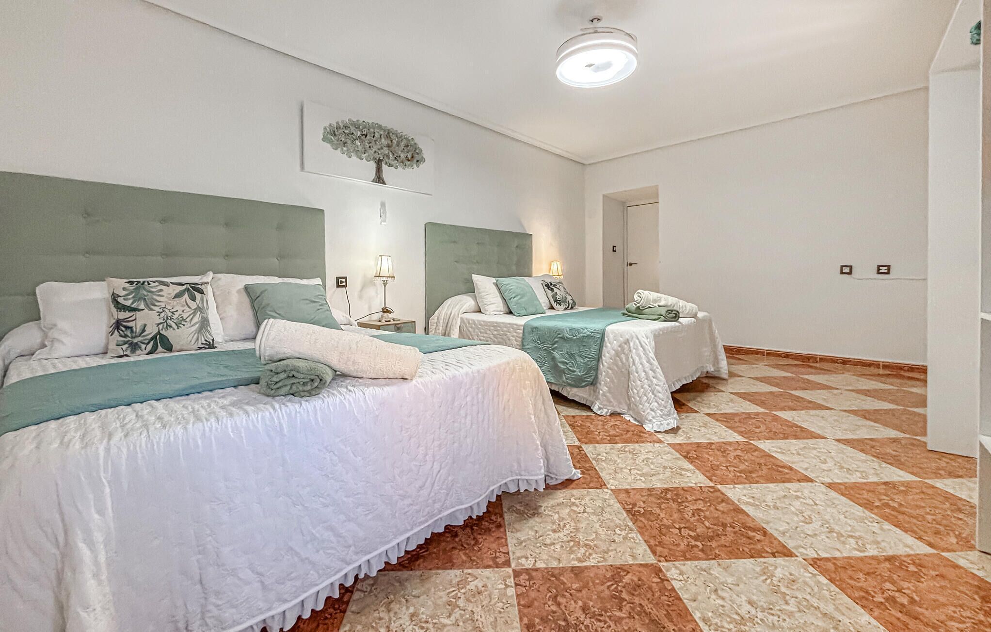 A hotel room with two beds, a ceiling light, and a wall-mounted artwork.