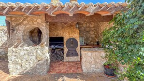 Una cocina exterior de piedra con suelo de baldosas, una chimenea y una planta en maceta.