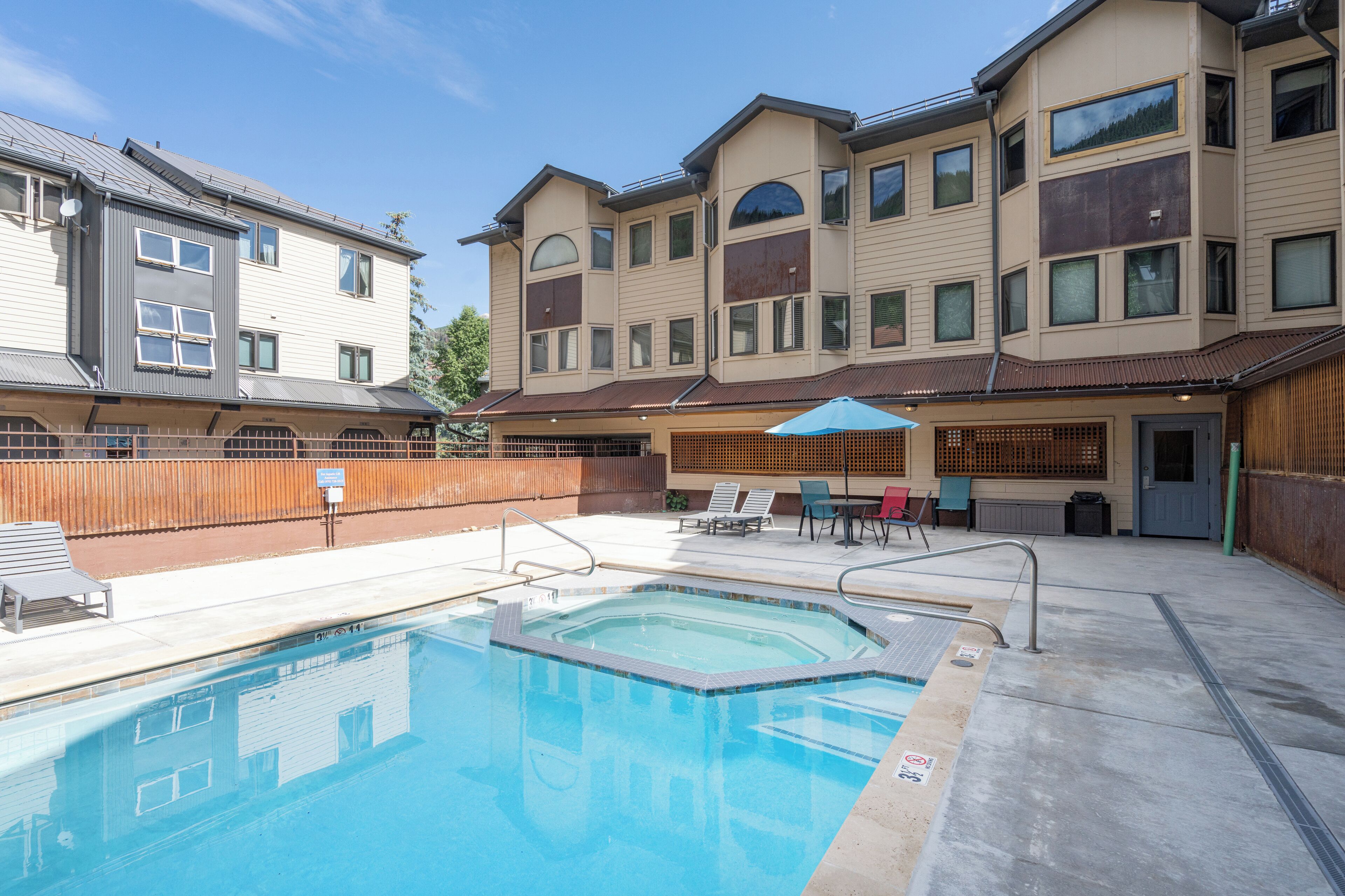A swimming pool with a wooden deck, lounge chairs, and a covered seating area.