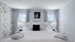 A neatly made bed with white bedding and a black pillow, two bedside lamps, and a wall-mounted picture. - The villa where dreams come true! (Davenport)