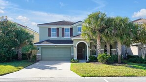 A two-story house with a garage, a front entrance with a door, and a driveway leading to the garage. - The villa where dreams come true! (Davenport)