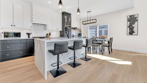 Une cuisine moderne avec des meubles blancs, un îlot central doté de tabourets et des luminaires suspendus.