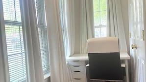 Ein Zimmer mit Schreibtisch, Stuhl und Fenster mit Jalousien.