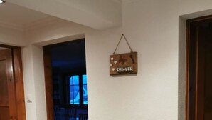 Un couloir avec une porte en bois sur la gauche, un mur en bois sur lequel est affiché un panneau indiquant « ZUHAUSE », et une pièce sombre au fond.