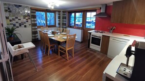 Une cuisine moderne avec des meubles en bois, une table à manger pour quatre personnes et une vue sur l’extérieur grâce à de grandes fenêtres.
