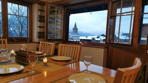 Une salle à manger avec une table en bois dressée pour quatre personnes, de grandes fenêtres donnant sur la ville et le clocher d’une église, et une bougie sur la table.