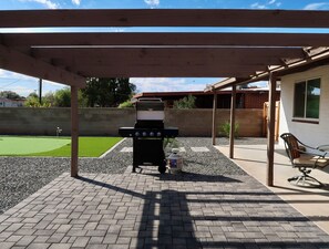 A covered patio with a grill, seating area, and a small lawn. - 3 Bedroom Retreat, 5 Min to AFB, Relaxing backyard! (Tucson)