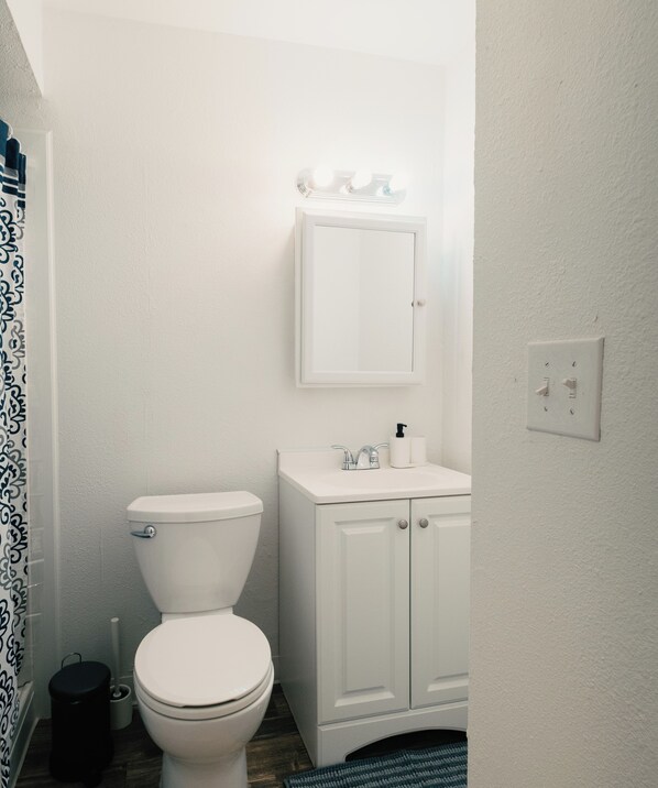 A small, white bathroom with a toilet, a cabinet, and a mirror with lights above it. - 3 Bedroom Retreat, 5 Min to AFB, Relaxing backyard! (Tucson)