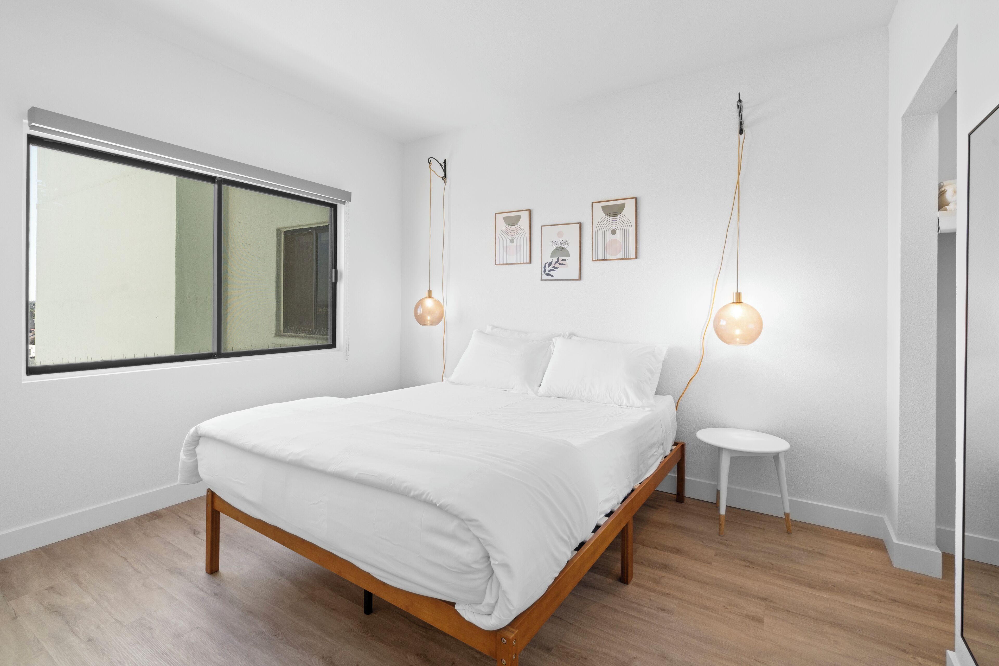 Un dormitorio moderno con una cama de madera, un ventanal grande y dos lámparas colgantes.