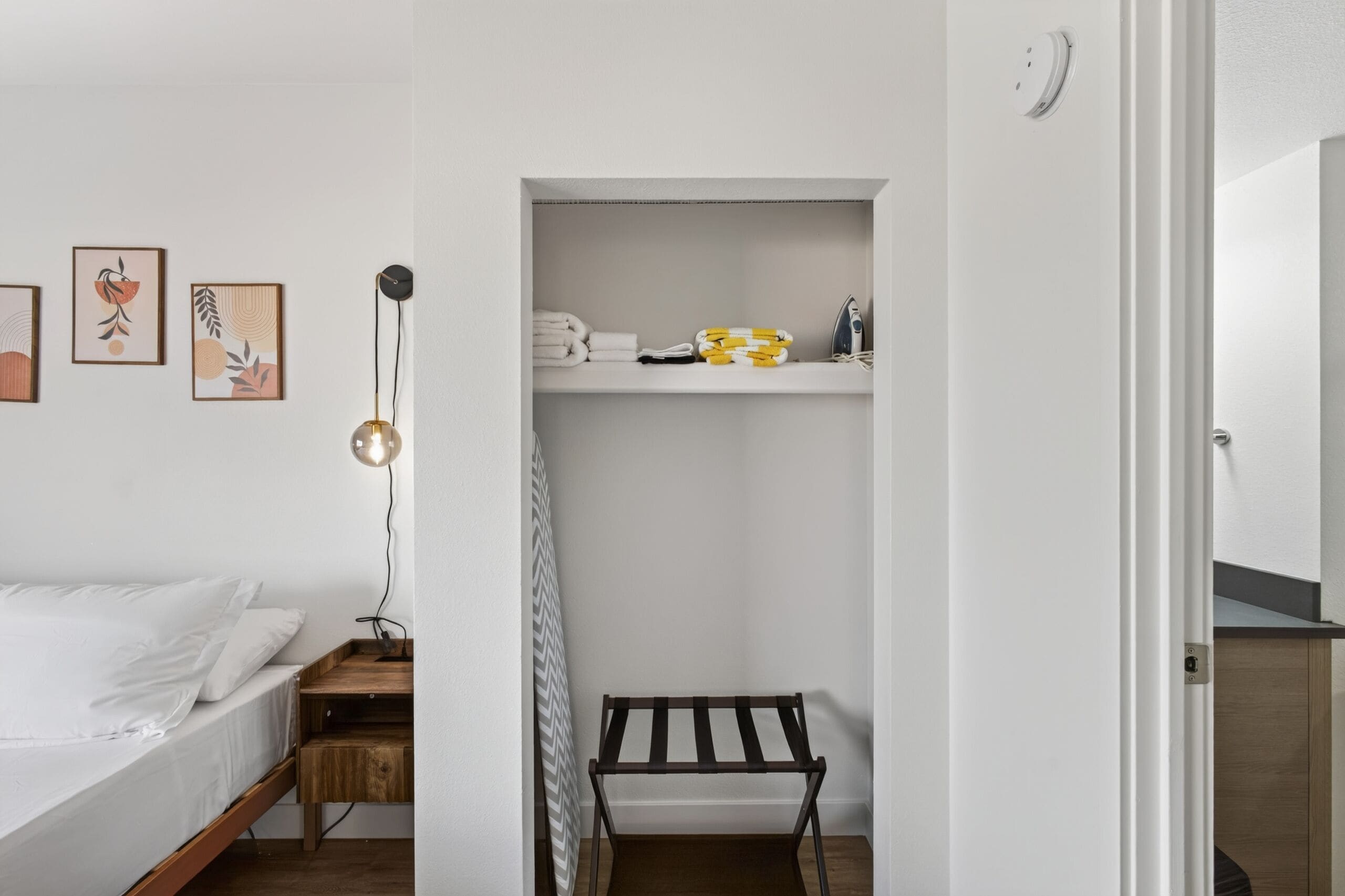 A compact bedroom with a bed, bedside table, lamp, and a small bench.
