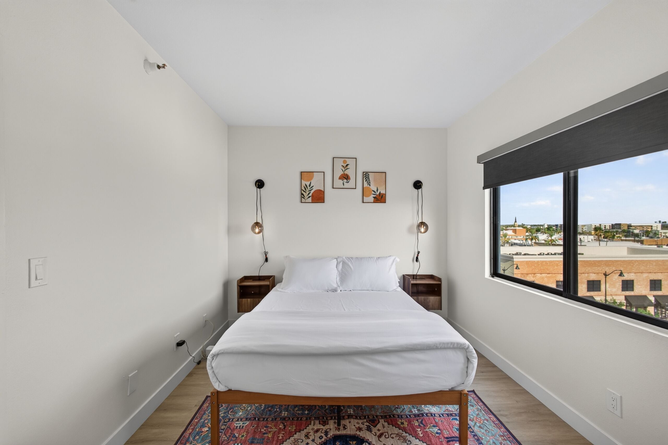 Ein Schlafzimmer mit großem Fenster, einem Bett, zwei Nachttischen und drei Wandleuchten.