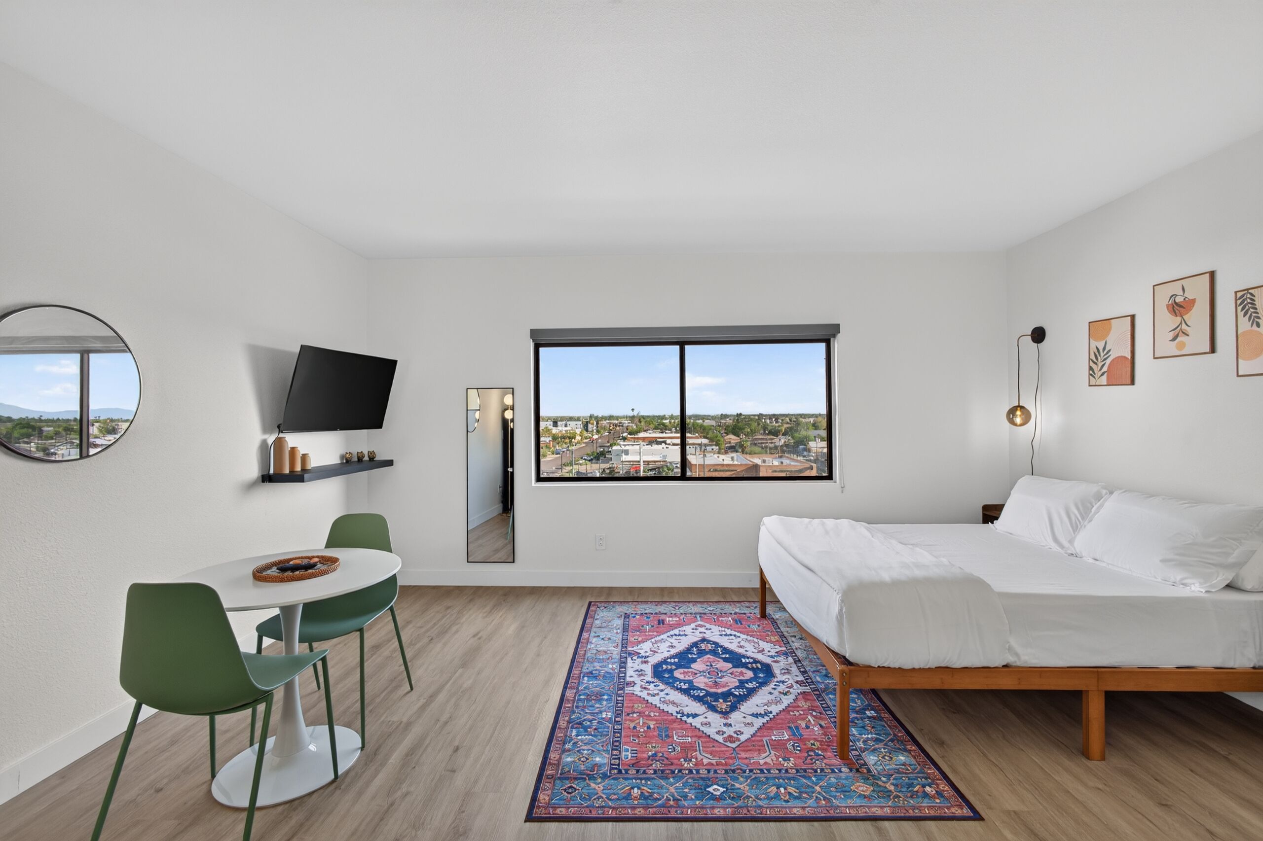 Una camera da letto moderna con un letto, una scrivania, una sedia, un'ampia finestra e vista sulla città.
