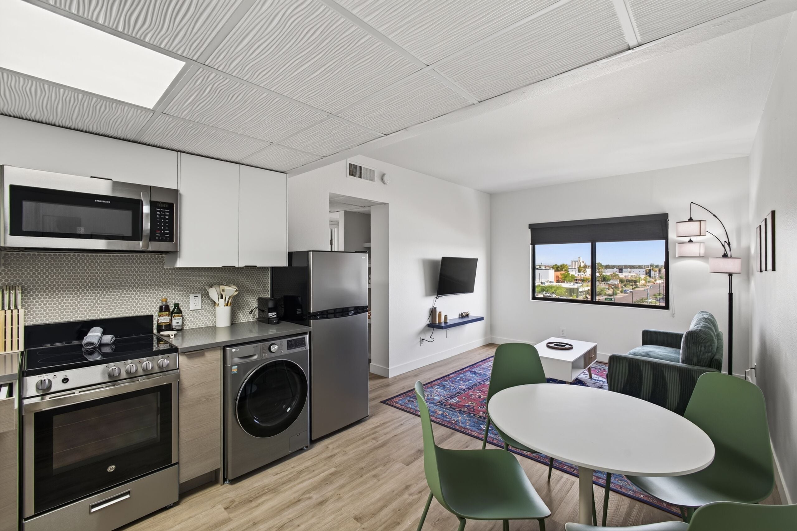 Una cocina moderna con electrodomésticos de acero inoxidable, lavadora y comedor con una mesa redonda y sillas verdes.