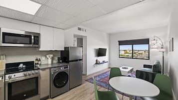 Una cocina moderna con electrodomésticos de acero inoxidable, lavadora y comedor con una mesa redonda y sillas verdes.