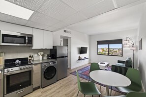 A modern kitchen with stainless steel appliances, a washing machine, and a dining area with a round table and green chairs. - Astral Desert Retreats (Mesa)