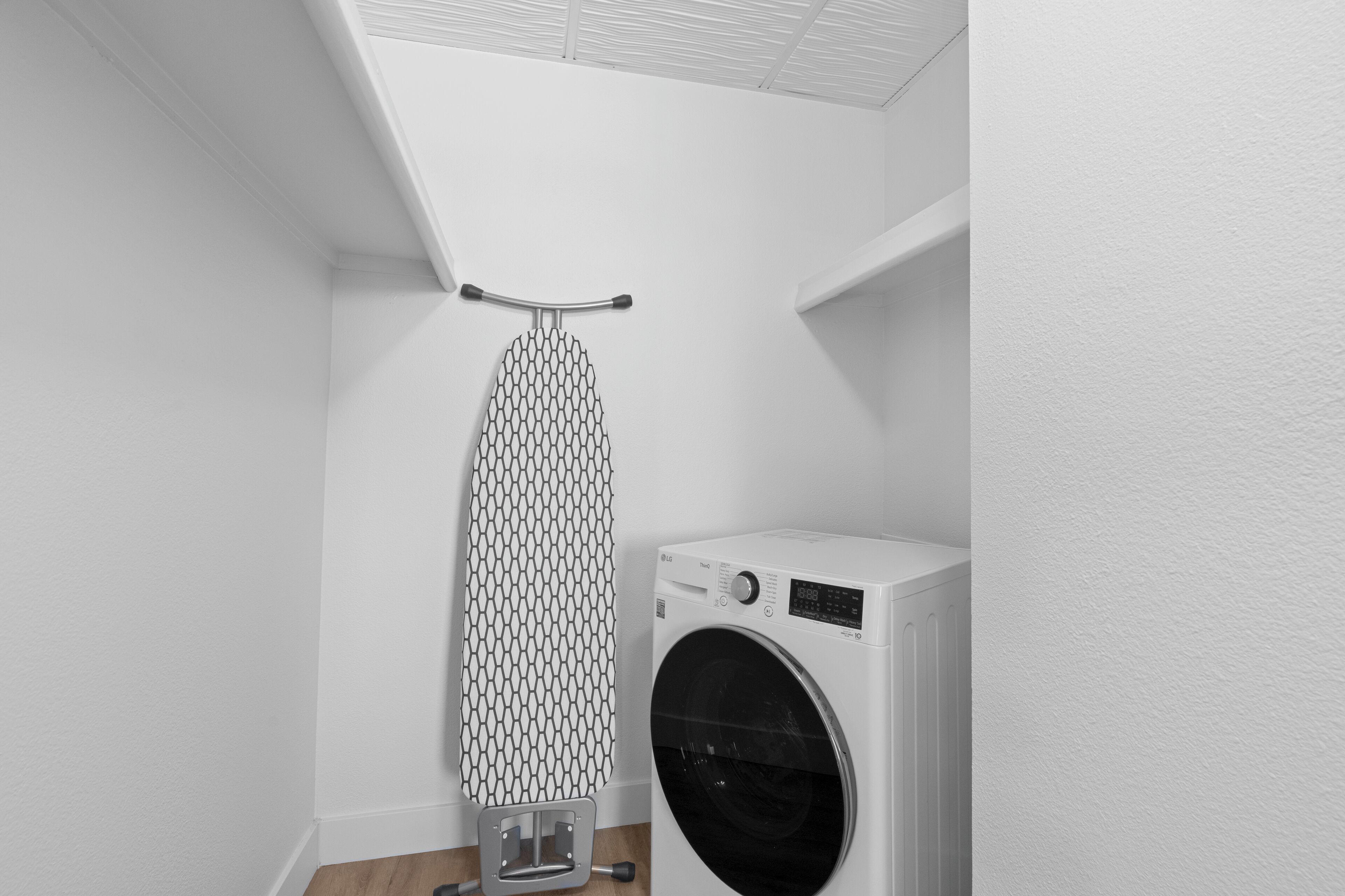 A laundry room with a wall-mounted iron rack and a front-loading washing machine.