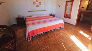 A bedroom with a bed, a nightstand, a chair, a wooden ceiling, and a tiled floor. - Cabañas El nido de la Huilota (Tepoztlan)
