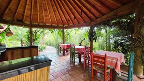 A covered outdoor area with a wooden ceiling, red and green tables, and chairs. - Cabañas El nido de la Huilota (Tepoztlan)