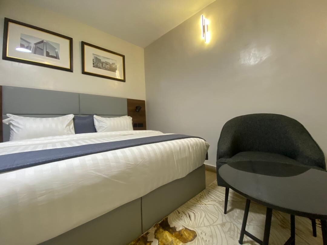 Una habitación de hotel con una cama, una silla y dos cuadros en la pared.