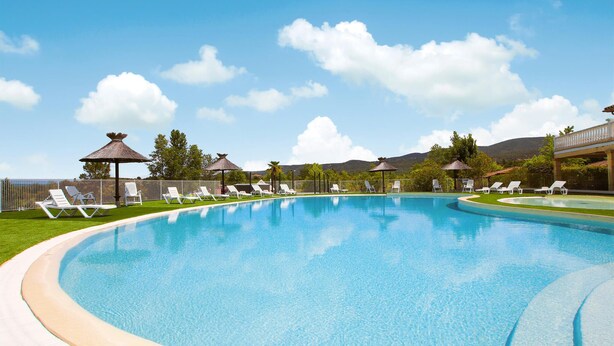 A swimming pool with lounge chairs and umbrellas, surrounded by a fence and trees, with a clear sky and mountains in the background. - Lovely home in Grospierres with WiFi (Grospierres)