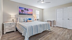 Ein Schlafzimmer mit Bett, Nachttischen, Deckenventilator, einem Gemälde und einem Kleiderschrank.