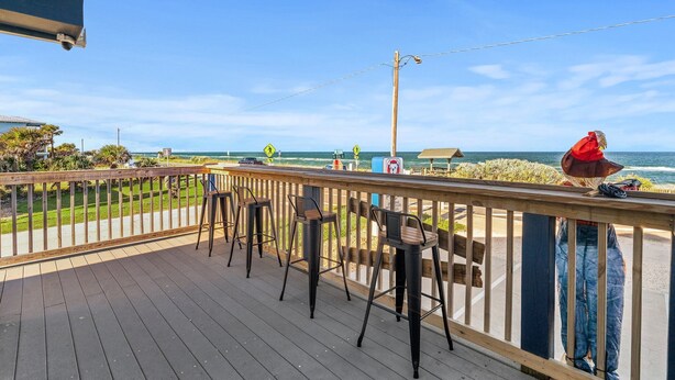 Eine Holzterrasse mit Metall-Barhocker und Blick auf den Ozean.