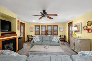 A living room with a sofa, a coffee table, a television, and a fireplace. - Shore Beats Work: Oceanfront Views, Pool, Hot Tub, Sauna, Discounted Golf Rates (Nags Head)