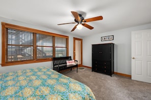 A bedroom with a bed, a ceiling fan, a bench, a wardrobe, and a door. - Shore Beats Work: Oceanfront Views, Pool, Hot Tub, Sauna, Discounted Golf Rates (Nags Head)