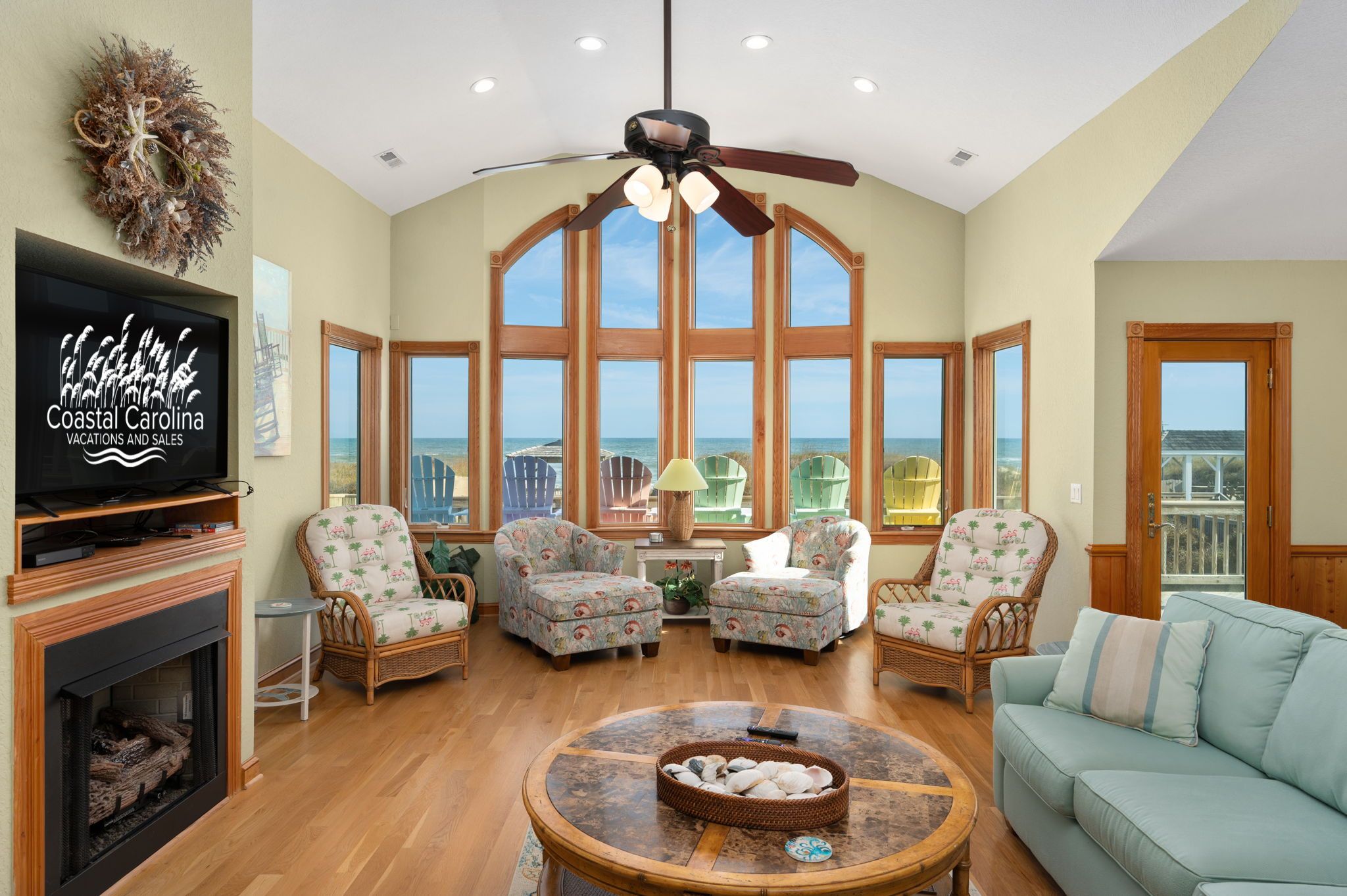 A spacious living room with a large TV, wicker furniture, and a view of the ocean.
