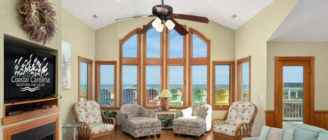 A spacious living room with a large TV, wicker furniture, and a view of the ocean.