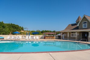 A swimming pool with lounge chairs and umbrellas, a bar area, and a building with a peaked roof. - 16 Sunset: Private Pool, Hot Tub, Game Room, Community Amenities (Corolla)