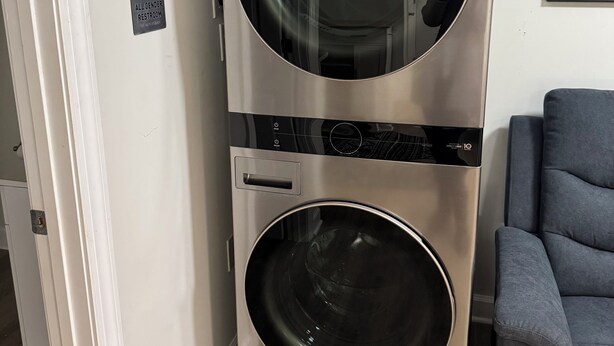 A stacked washer and dryer unit in a room with a gray couch and a framed picture on the wall. - Charming & luxurious 1-bedroom condo, Kitchen, Washer, dryer, parking, King Bed. (Hagerstown)