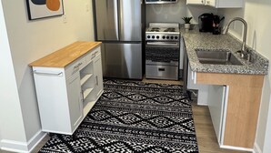A compact kitchen with white cabinets, stainless steel appliances, a wooden countertop, and a patterned rug. - Charming & luxurious 1-bedroom condo, Kitchen, Washer, dryer, parking, King Bed. (Hagerstown)