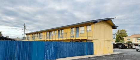 A yellow building with a blue fence, a parking lot, and a cloudy sky.