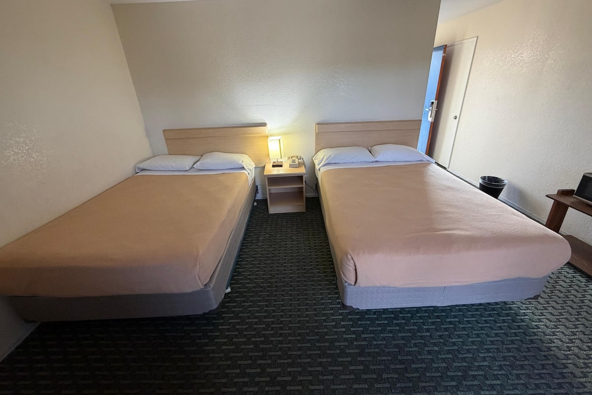 A hotel room with two single beds, a nightstand with a lamp, and a small table with a television.