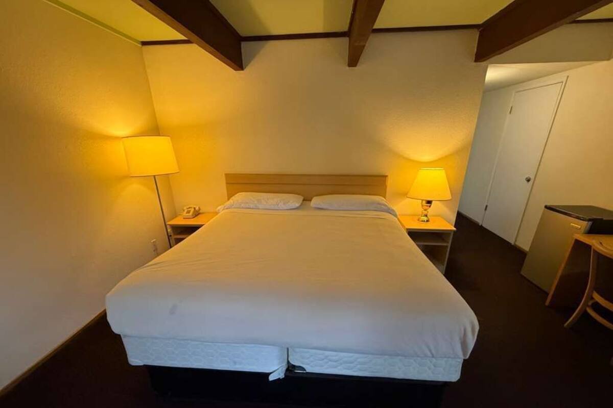 A hotel room with a large bed, two bedside lamps, a nightstand, and a desk with a chair.