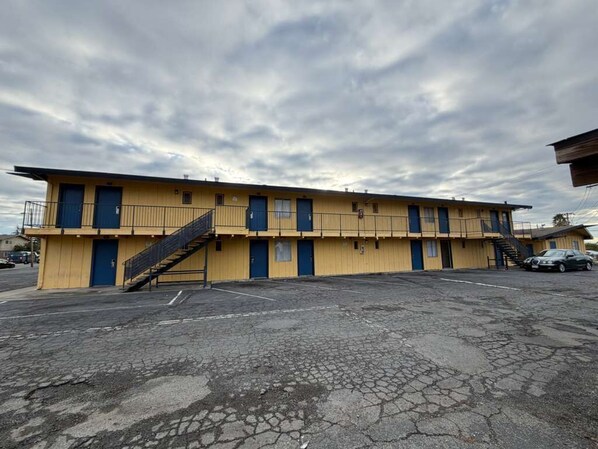A yellow motel with multiple rooms, a parking lot, and a staircase leading to the upper floors. - Royal plams  (Concord)