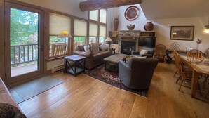 Amplia sala de estar con chimenea, muebles de madera, una mesa de comedor con sillas y ventanas grandes que ofrecen vistas al exterior.