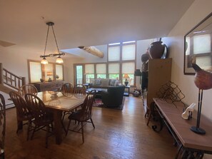 A spacious living area with a dining table, chairs, a sofa, and a kitchen area in the background.