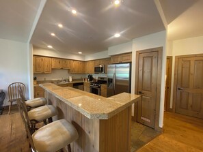 A kitchen with wooden cabinets, a stainless steel refrigerator, a microwave, and a granite countertop.