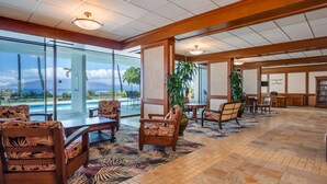 Un hall d’entrée spacieux avec vue sur la piscine, des meubles en bois et une moquette aux motifs tropicaux.