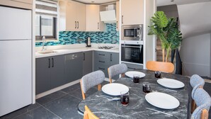 A modern kitchen with grey cabinets, a stainless steel microwave, and a dining area with a marble table and grey upholstered chairs. - Sun, sea, and serenity — your perfect Kalkan getaway (Kalkan Centre)