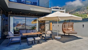 A modern outdoor patio with a dining set, a lounge chair, and a large umbrella. - Sun, sea, and serenity — your perfect Kalkan getaway (Kalkan Centre)