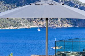 Blick von einem Balkon auf das klare, blaue Meer, eine felsige Küste und Segelboote.