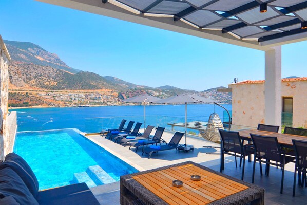 A poolside area with lounge chairs and a table, overlooking a coastal landscape with mountains and a clear sky. - Discover your Kalkan escape – private pool and sea views (Kalkan Centre)