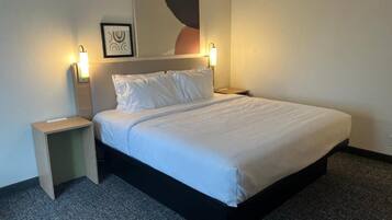 A hotel room with a bed, two bedside tables, a wall-mounted light, and a framed picture.